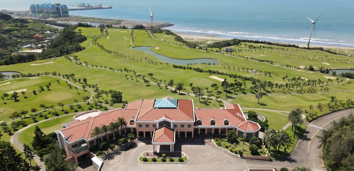 Aerial view of Pali International clubhouse with red roofs, fairways and the sea beyond